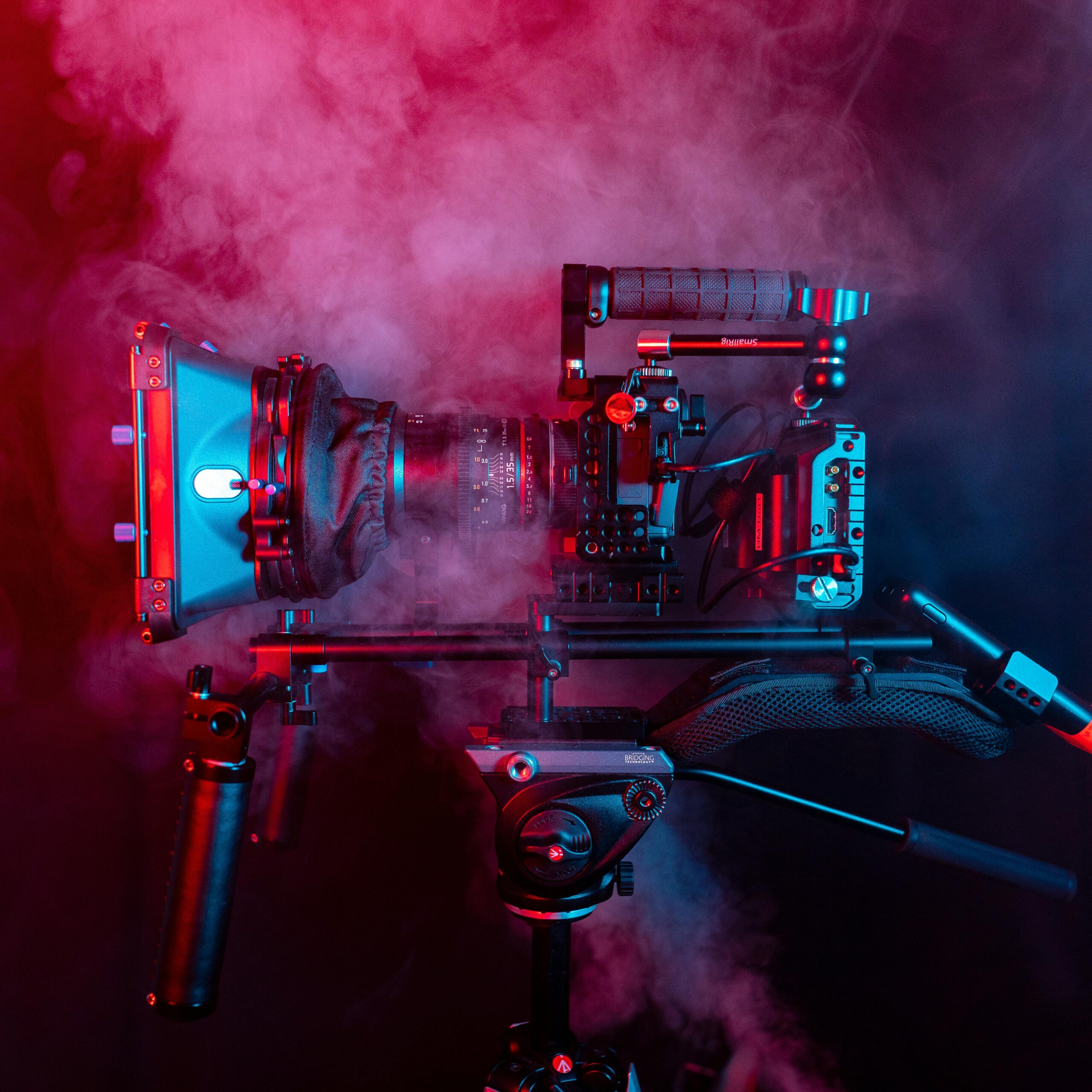 Professional cinematic camera with a shoulder rig surrounded by red and blue smoke.